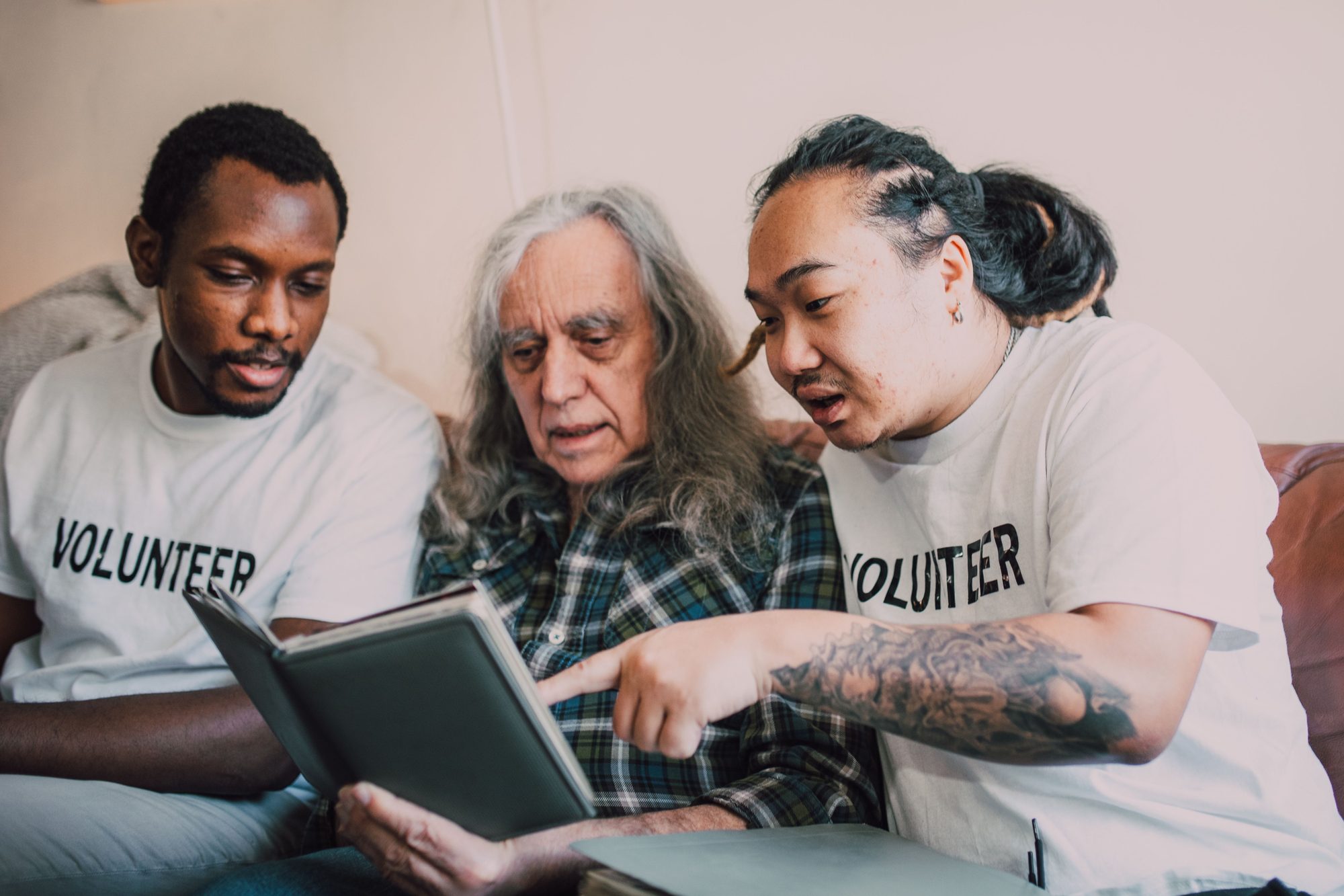 Two volunteers sit with an older man on a sofa, looking through a photo album together during a companion visit
